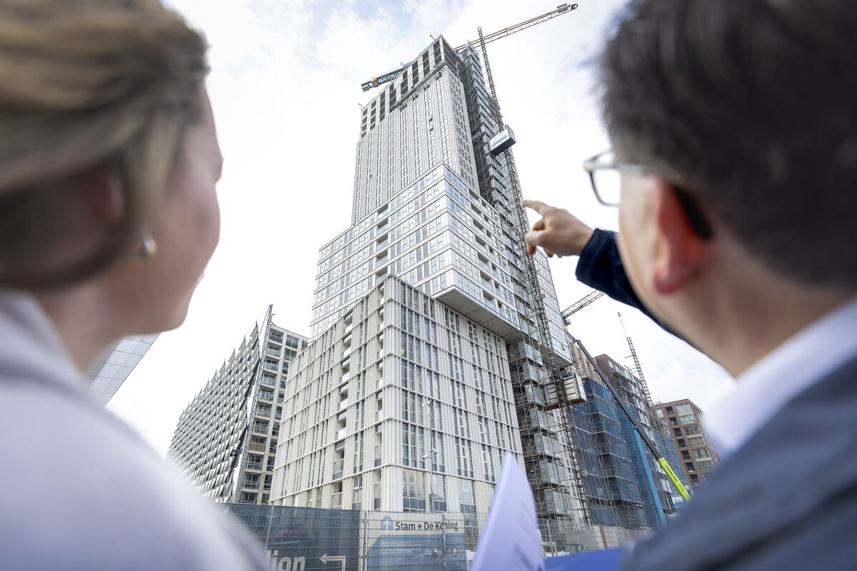 Man and woman look up at grey skyscraper under construction.